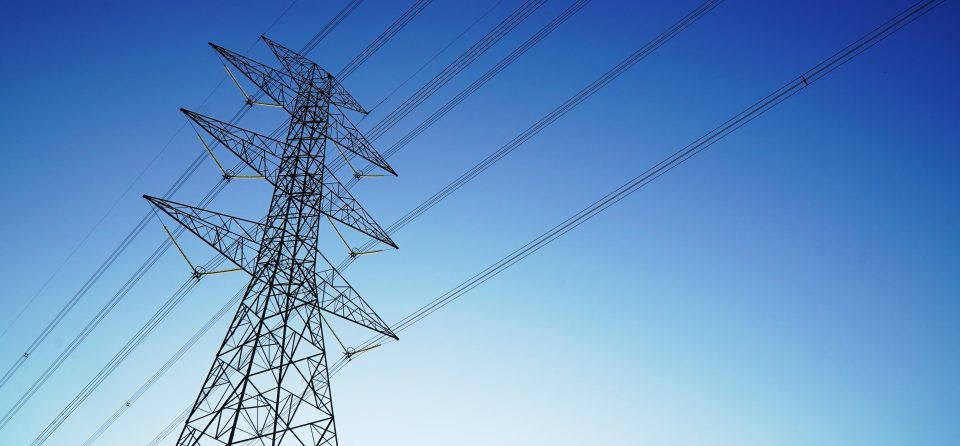 Foto van een netwerk van hoogspanningskabels met een blauwe ochtendlucht op de achtergrond.